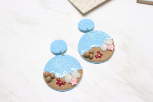 Pair of earrings with beach-themed design on a white surface